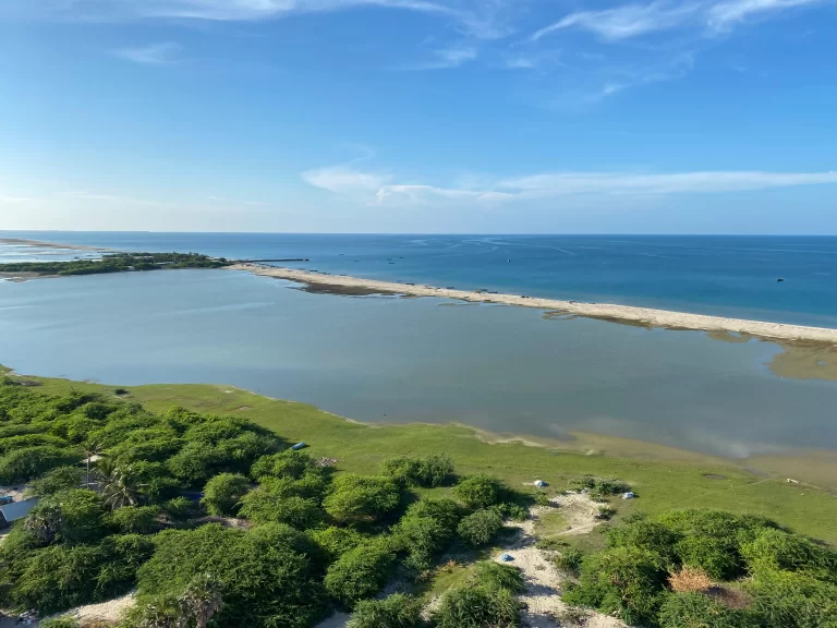 Aerial view of a coastal landscape featuring water, sand, and greenery under a clear blue sky.
